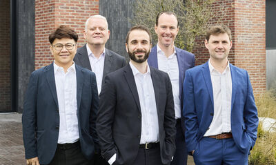 Five team members in suits standing together in front of a brick building