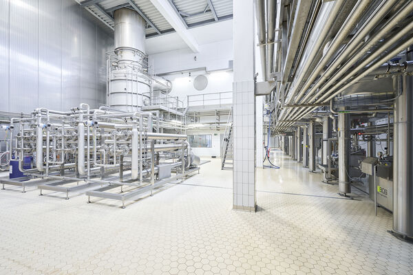 Bright industrial hall with stainless steel processing tanks, pipework and tiled floor