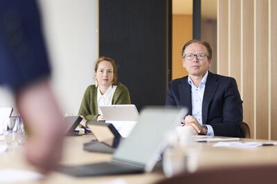 Man with glasses and a woman attending a meeting in a wood-panelled boardroom