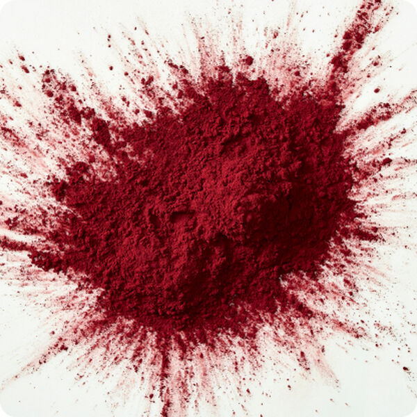 Deep red spray-dried protein powder bursting outward on a white surface