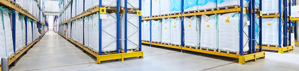 Warehouse aisle with white big-bags of feed ingredients stacked on tall blue pallet racks