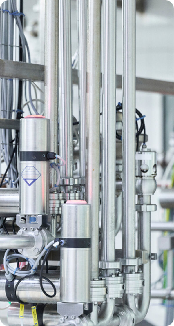 Close-up of polished stainless steel processing pipes and sensors in a feed plant