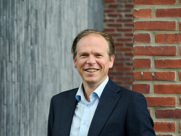 Smiling team member in a navy blazer and light blue shirt in front of a brick wall