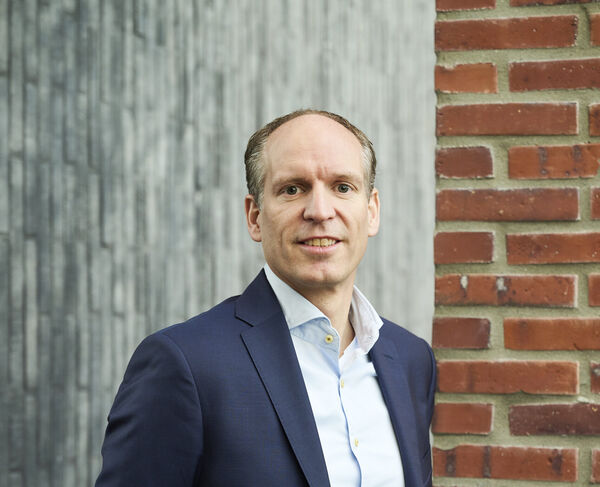 Team member in a blue blazer and light blue shirt in front of a concrete and brick wall