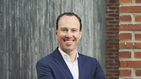 Smiling team member in a blue blazer and white shirt in front of a concrete and brick wall