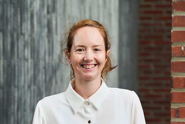 Portrait of Shirley Rousseau in a white blouse against a grey wood and brick wall